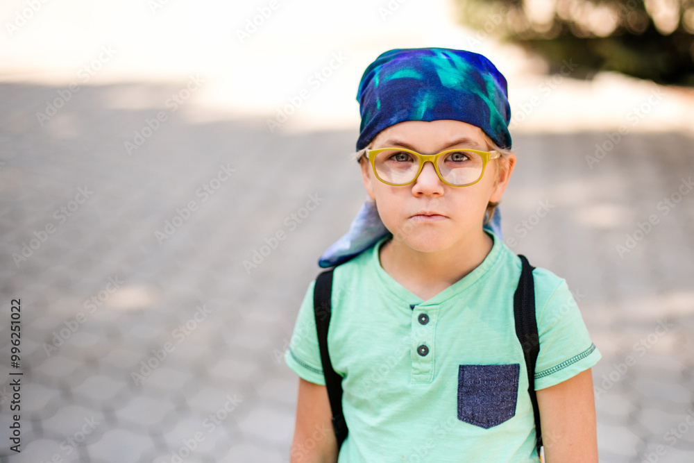 A funny little boy in glasses and a bandana, wearing a green t-shirt and denim shorts, having fun and joking A funny little boy in glasses and a bandana, wearing a green t-shirt and denim shorts, having fun and joking