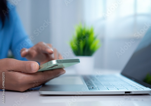 Businesswoman hand with a mobile phone over a laptop, Workplace at home, Freelancer, Working sitting in office at home, Online shopping and payments, Ecommerce and secure mobile banking concept.