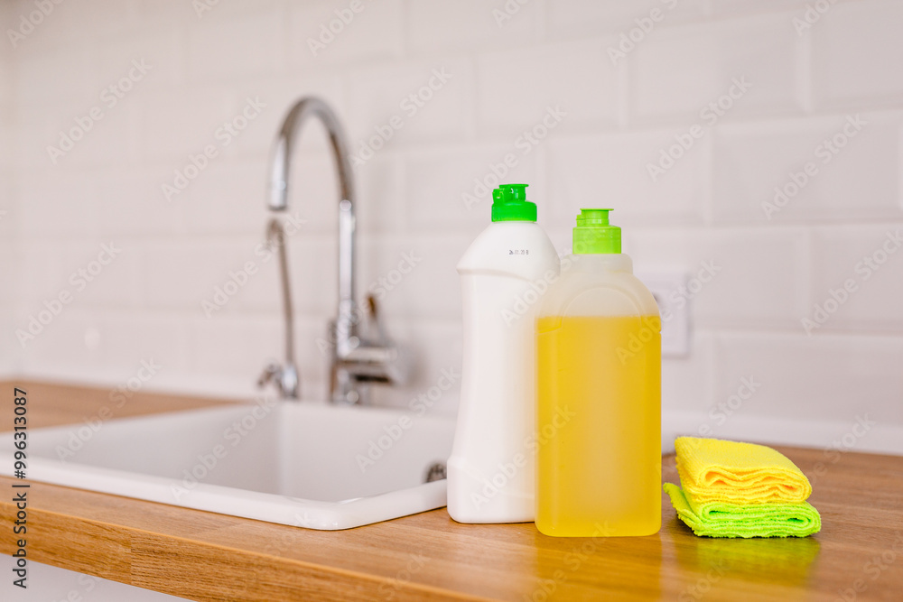 White plates, glass cups and forks in a clean white sink and two bottles of detergent and microfiber rags on a wooden table in a white kitchen White plates, glass cups and forks in a clean white sink and two bottles of detergent and microfiber rags on a wooden table in a white kitchen
