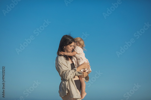 Smiling mother and beautiful daughter having fun on the beach. Portrait of kid embracing her mom during summer. photo