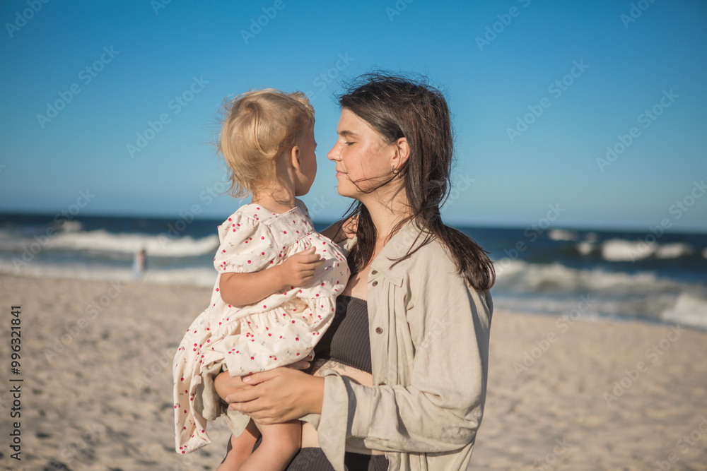 Smiling mother and beautiful daughter having fun on the beach. Portrait of kid embracing her mom during summer.