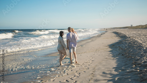 A young perents holds her little daughter by the hand and together they walk along the ocean towards the sunset. photo