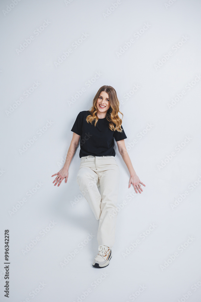 A pretty woman in a black t-shirt and white pants on a white background. Smiling woman in casual clothes on a white background. A pretty woman in a black t-shirt and white pants on a white background. Smiling woman in casual clothes on a white background.