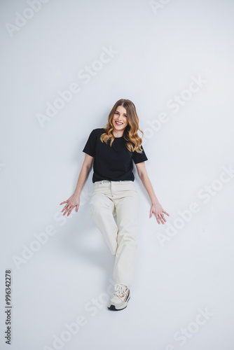 A pretty woman in a black t-shirt and white pants on a white background. Smiling woman in casual clothes on a white background.