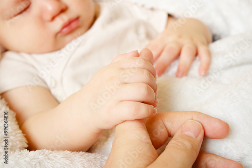baby holding adult's finger while sleeping