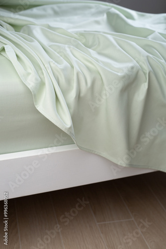 A light green cotton sheet lying carelessly on the bed. Close-up, macro photo. Minimalist bedroom. Cozy home concept. Scandinavian style