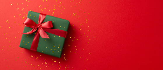 A beautifully wrapped green gift box with a vibrant red ribbon on a red background, perfect for Christmas or special occasions