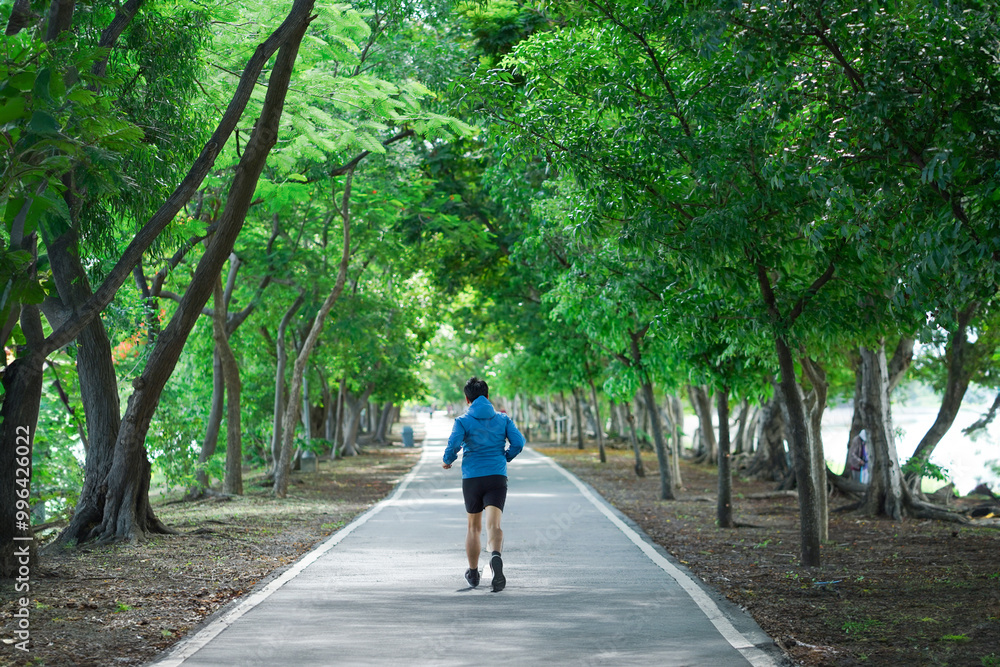 A man is running on a path in a park. The path is surrounded by trees and there are benches along the way. The man is wearing a blue jacket and black shorts. The scene is peaceful and serene A man is running on a path in a park. The path is surrounded by trees and there are benches along the way. The man is wearing a blue jacket and black shorts. The scene is peaceful and serene