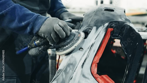 A technician sands a car's bodywork at an auto repair shop in the early morning