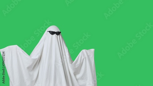 Funny halloween ghost in white sheet wears black glasses dancing coolly, isolated on chroma key green screen background. Happy halloween spooky concept.