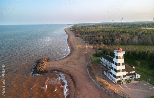 West Point lighthouse stands prominently on the coastline as the sun sets over the calm ocean waters, illuminating the sky with vibrant hues of orange and yellow, Prince Edward Island, Canada photo