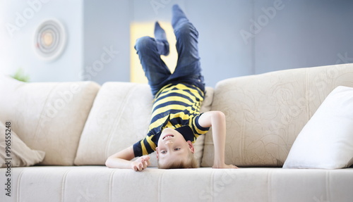 Photography Portrait of young boy child standing on head on beige sofa going crazy at home on holiday