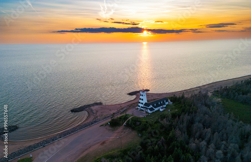 West Point lighthouse stands prominently on the coastline as the sun sets over the calm ocean waters, illuminating the sky with vibrant hues of orange and yellow, Prince Edward Island, Canada photo