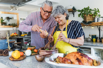 Latin senior couple cooking a turkey meat together for Christmas dinner at home in Mexico Latin America, hispanic people preparing food in thanksgiving holidays	