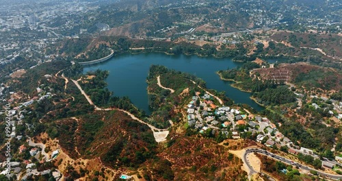 View on the Hollywood Reservoir in the rocky mountains. Drone descending above the scenery on sunny daytime. Lots of cottages are on the hills.