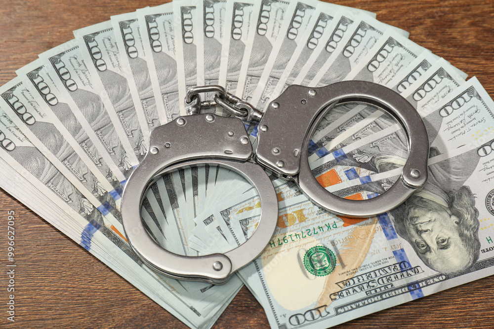 Handcuffs with dollar banknotes on wooden table Handcuffs with dollar banknotes on wooden table
