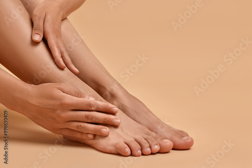 Woman touching her smooth feet on beige background, closeup