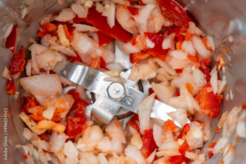 Chopped garlic, onion, and red bell pepper inside a food processor, ready for cooking. Fresh ingredients prepared for a flavorful dish, vibrant and colorful kitchen scene. photo