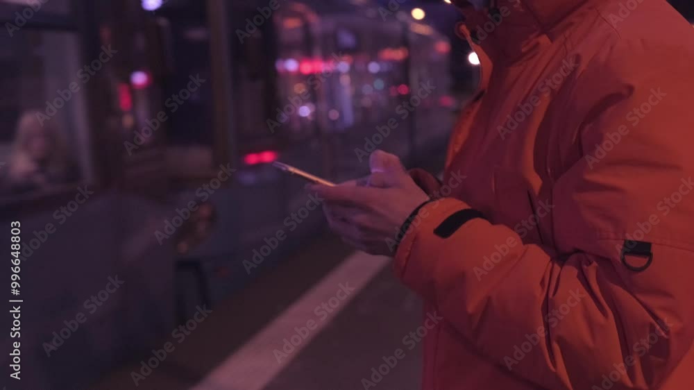 Twilight on platform above-ground metro station, man holds his phone in the dark, with lights of traffic, city and passing trains in background, person in subway, immersed in phone, Nightlife Twilight on platform above-ground metro station, man holds his phone in the dark, with lights of traffic, city and passing trains in background, person in subway, immersed in phone, Nightlife