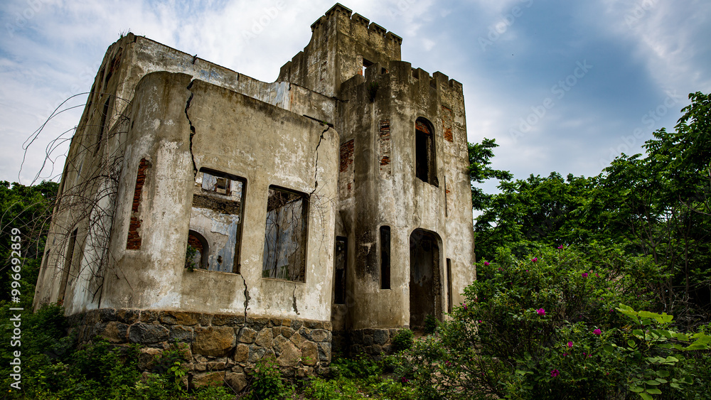 An old building with few windows is enclosed by trees and bushes An old building with few windows is enclosed by trees and bushes