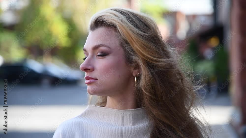 Close-up portrait of beautiful long haired caucasian blond woman in white sweater standing outdoor on city street in a summer or autumn morning. Soft focus. Beautiful people and fashion theme. Close-up portrait of beautiful long haired caucasian blond woman in white sweater standing outdoor on city street in a summer or autumn morning. Soft focus. Beautiful people and fashion theme.