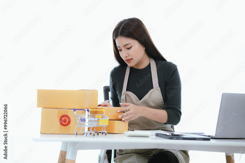 A happy Asian entrepreneur manages her online store from her home office, ensuring smooth logistics and satisfied customers in her growing startup. A happy Asian entrepreneur manages her online store from her home office, ensuring smooth logistics and satisfied customers in her growing startup.