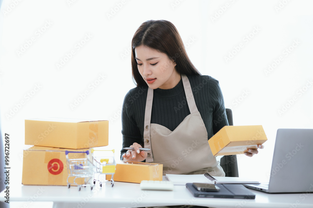 A happy Asian entrepreneur manages her online store from her home office, ensuring smooth logistics and satisfied customers in her growing startup. A happy Asian entrepreneur manages her online store from her home office, ensuring smooth logistics and satisfied customers in her growing startup.