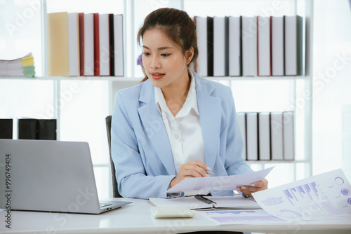 Confident and charming Asian businesswoman using laptop and smartphone. She is full of professionalism and achievement in data analysis, effective communication and organizational management in modern