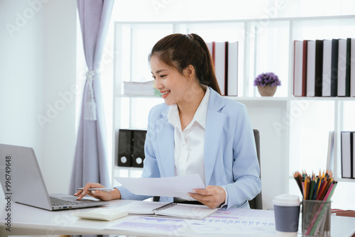 Confident and charming Asian businesswoman using laptop and smartphone. She is full of professionalism and achievement in data analysis, effective communication and organizational management in modern