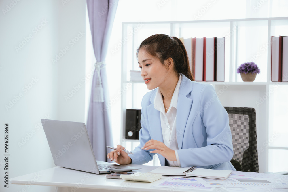 Confident Asian businesswoman in modern office smiling while working on laptop, analyzing reports, planning marketing strategies and leading with energy and positivity. Confident Asian businesswoman in modern office smiling while working on laptop, analyzing reports, planning marketing strategies and leading with energy and positivity.