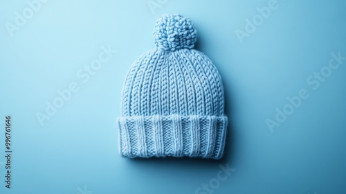 This neatly folded winter hat in soft pastel blue showcases its knitted texture and round pom-pom, perfectly complementing the serene backdrop