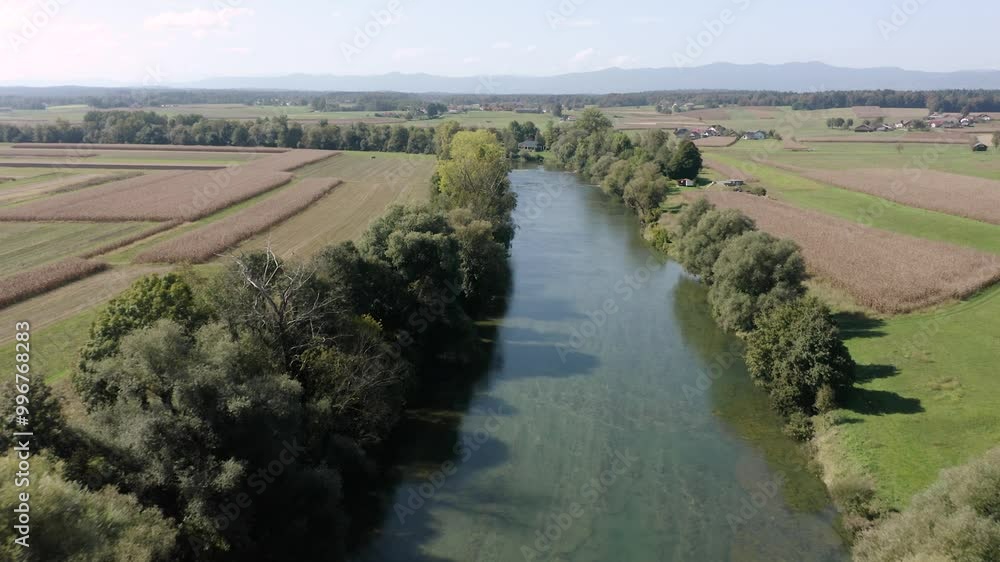 An aerial view of a river Kolpa winding through expansive farmland, with lush trees lining the riverbank. Clear skies stretch above distant mountains, and fields surround the flowing water. An aerial view of a river Kolpa winding through expansive farmland, with lush trees lining the riverbank. Clear skies stretch above distant mountains, and fields surround the flowing water.