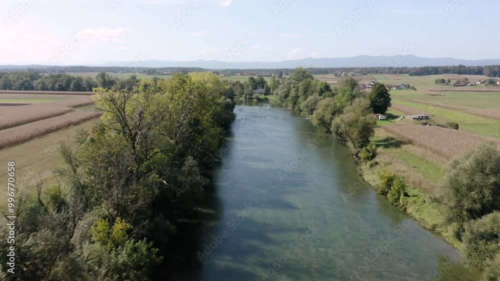 Flying above calm river Kolpa flowing gently between thick clusters of trees. A small rural house sits along the riverbank, surrounded by greenery and peaceful countryside. Flying above calm river Kolpa flowing gently between thick clusters of trees. A small rural house sits along the riverbank, surrounded by greenery and peaceful countryside.