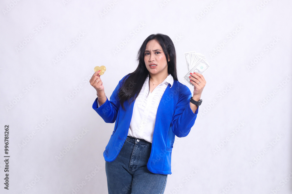 Elegant adult office girl wearing blue formal suit standing angry to camera hand holding dollar money and bitcoin isolated white background. for transaction, investment, business content