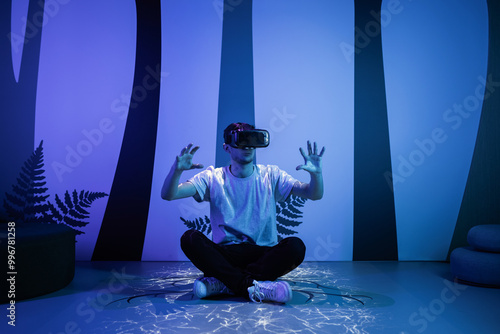 Young man wearing VR glasses sitting in a yoga pose on the virtual reality escape room floor. Fun, entertainment, and innovation concepts. photo