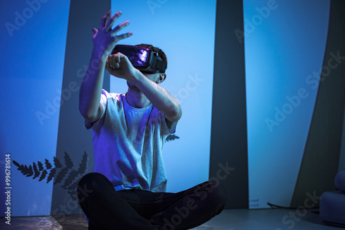 Young man wearing VR glasses sitting in a yoga pose on the virtual reality escape room floor. Fun, entertainment, and innovation concepts. photo