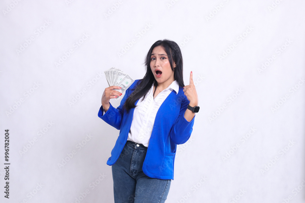 beautiful mature office woman wearing blue formal suit standing surprised to camera holding dollar bill to right and pointing up isolated white background. for transaction, finance, business content beautiful mature office woman wearing blue formal suit standing surprised to camera holding dollar bill to right and pointing up isolated white background. for transaction, finance, business content