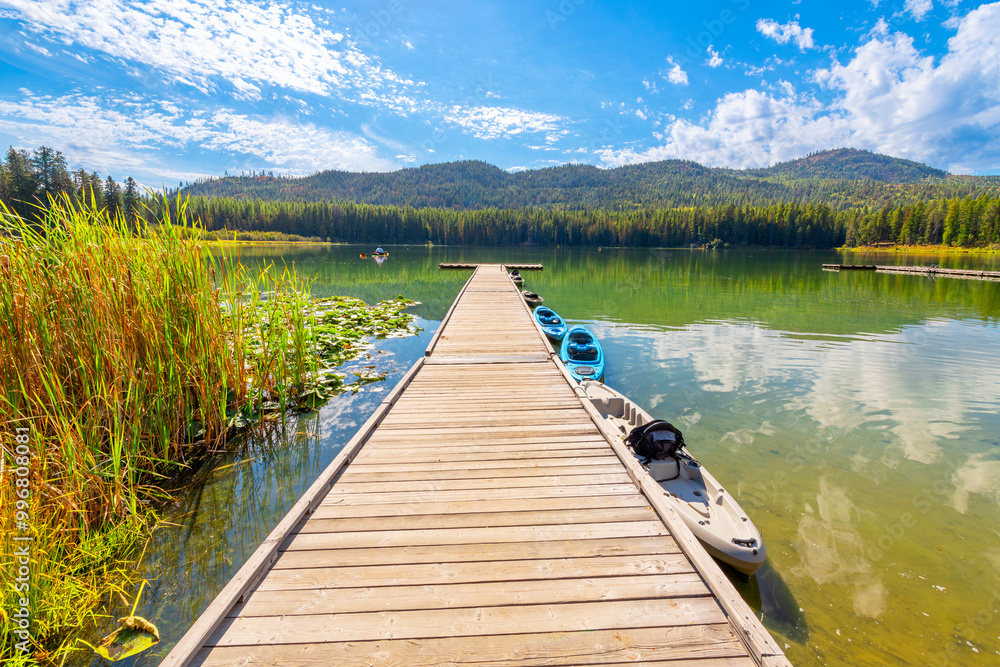 Fototapeta premium A man in a kayak boats from a wooden dock with more kayaks moored to it on Round Lake, one of the small natural lakes in the panhandle region of Coeur d'Alene, Idaho USA.