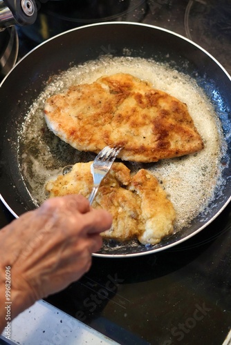 Close-up of an elderly woman's hand frying cutlets in a pan