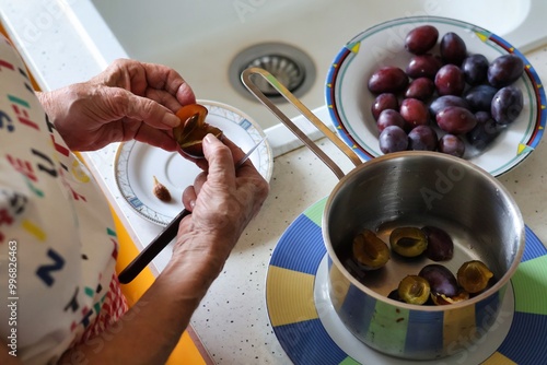 Close-up of the hands of an elderly woman peeling plums and throwing them into a pot to prepare jam