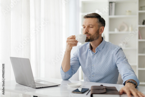 Fotografia A man with a beard sits at a desk, savoring a cup of coffee