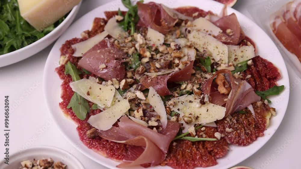 Close-up of appetizing appetizer carpaccio of figs, prosciutto, arugula and parmesan sprinkled with walnuts on a plate Close-up of appetizing appetizer carpaccio of figs, prosciutto, arugula and parmesan sprinkled with walnuts on a plate