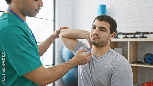 Physiotherapist evaluating shoulder joint of a male patient in a modern rehabilitation clinic.