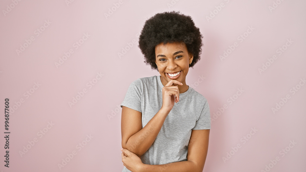 Smiling african american woman with curly hair posing against a pink background in a casual gray shirt. Smiling african american woman with curly hair posing against a pink background in a casual gray shirt.