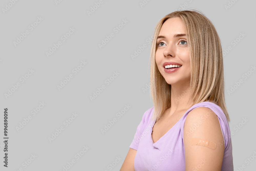 Young woman with medical patch on arm against grey background. Vaccination concept Young woman with medical patch on arm against grey background. Vaccination concept