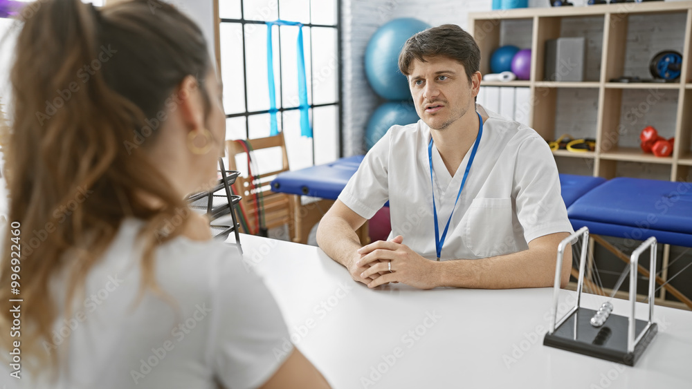A male physiotherapist consults with a female patient in a modern rehab clinic room. A male physiotherapist consults with a female patient in a modern rehab clinic room.
