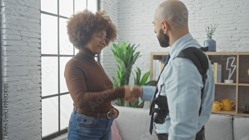 A man and woman with diverse ethnic backgrounds shaking hands in a bright, modern office setting, implying a professional collaboration. photo