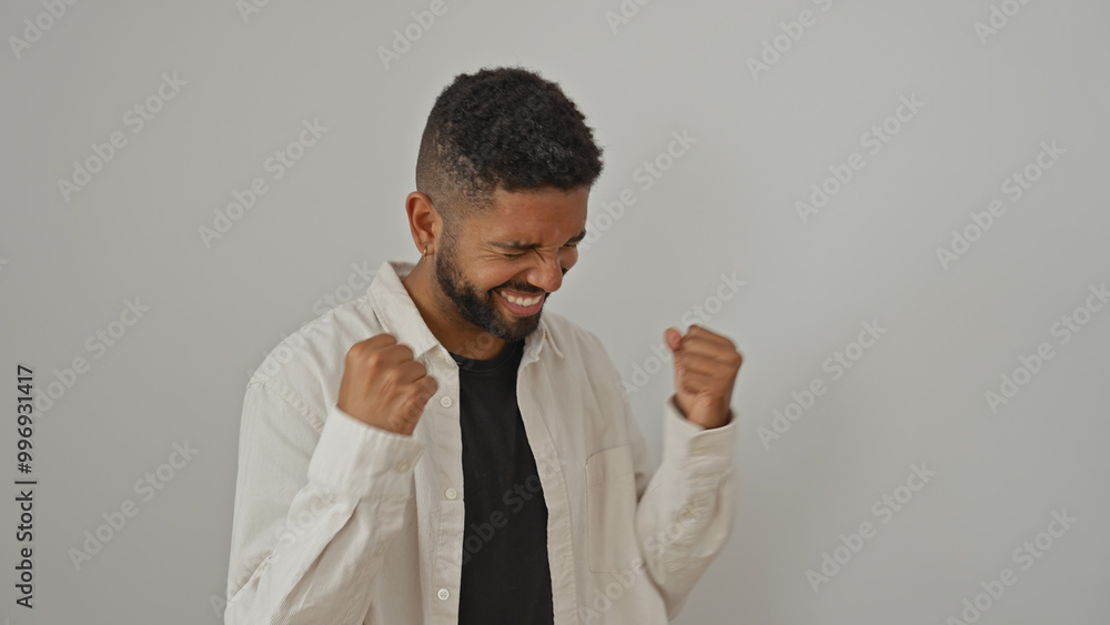 A young black man in a white shirt celebrates with clenched fists against a white background A young black man in a white shirt celebrates with clenched fists against a white background