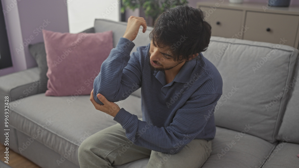 A young man experiencing elbow pain sitting in a modern living room A young man experiencing elbow pain sitting in a modern living room