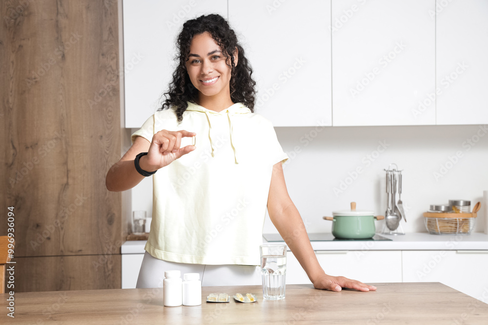 Young African-American woman taking fish oil in kitchen Young African-American woman taking fish oil in kitchen